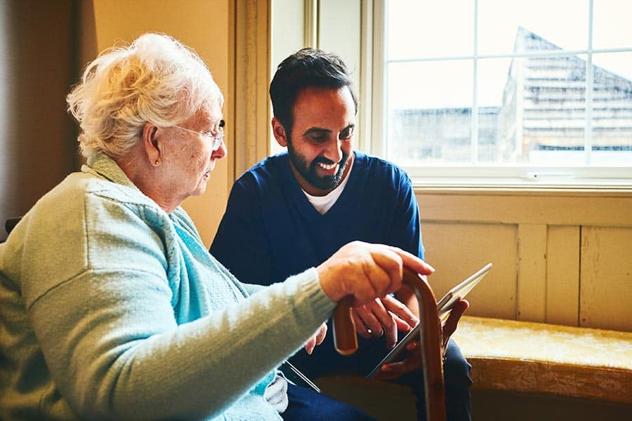 Male nurse showing a digital tablet to an elderly woman in a care home.