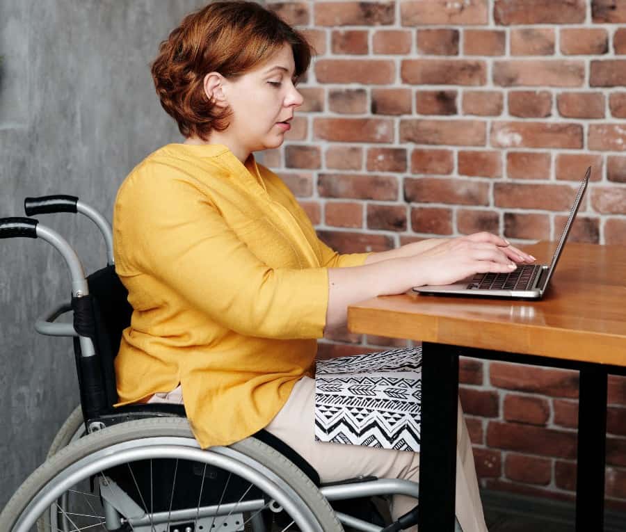 Lady in wheelchair uses a laptop on a table at home.